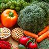 Un colorato assortimento di verdure a foglia verde, bacche e noci su un tagliere in legno, simbolo di alimentazione vegetale.